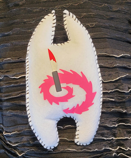A black fringed fabric pouch or organizer with a white shell-shaped patch featuring a pink spiral and a red-and-black arrow, photographed indoors on a dark surface.