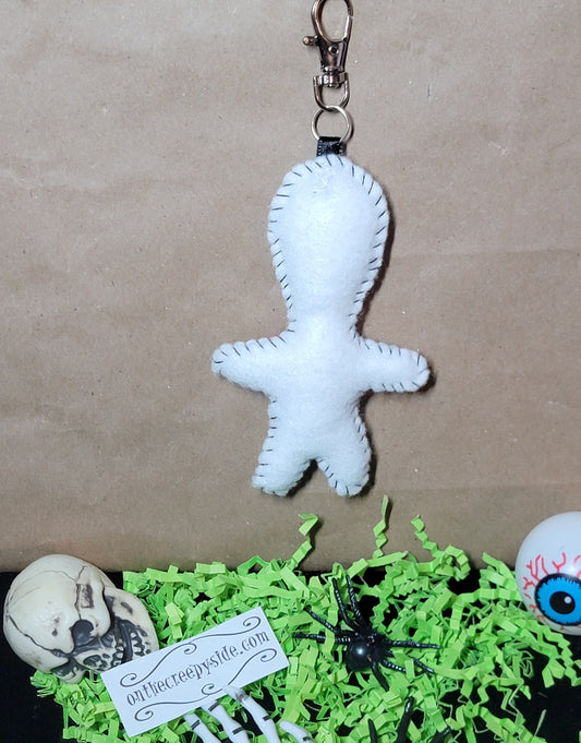 Back view of handmade white felt Rock Star Stitchling keychain showing black hand-stitched edging and metal clip