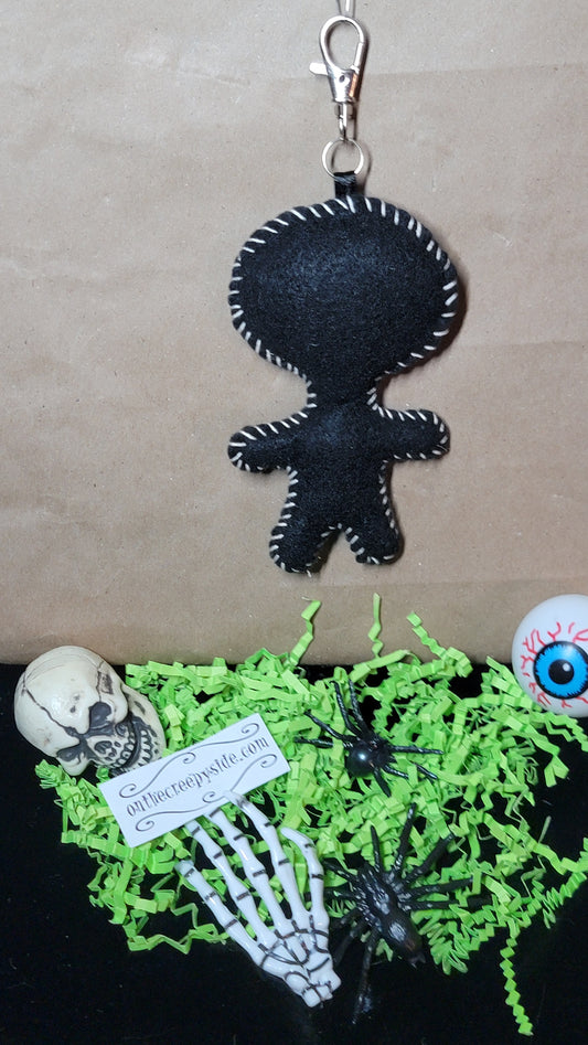 Back view of handmade black felt Mini Music Mascot Eddie Stitchling keychain with white hand-stitched edging and metal clip