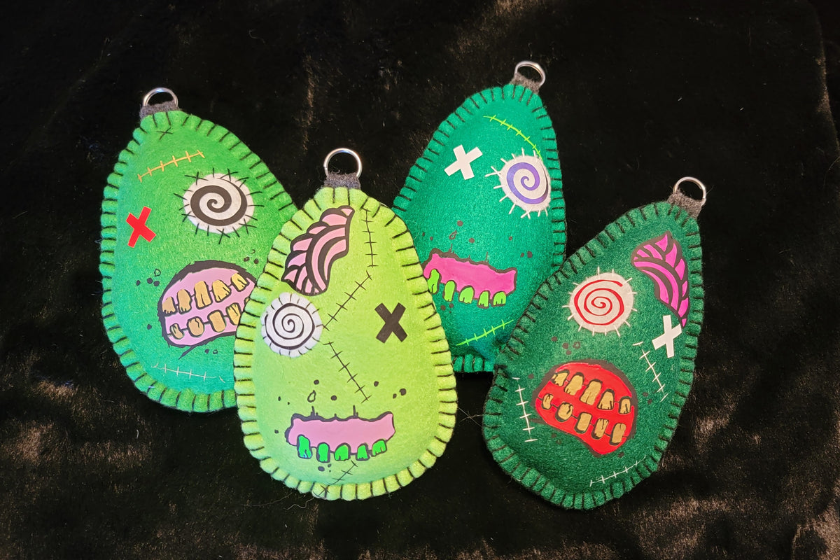 Four green felt keychains with colorful designs on a dark background