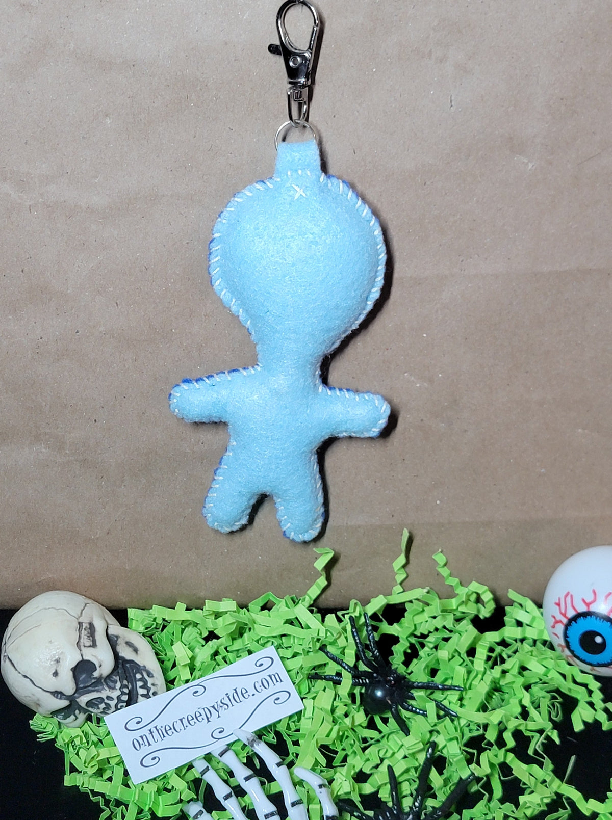 Back view of handmade pale blue felt mummy Rock Mascot Stitchling keychain with blue hand-stitched edging and metal clip