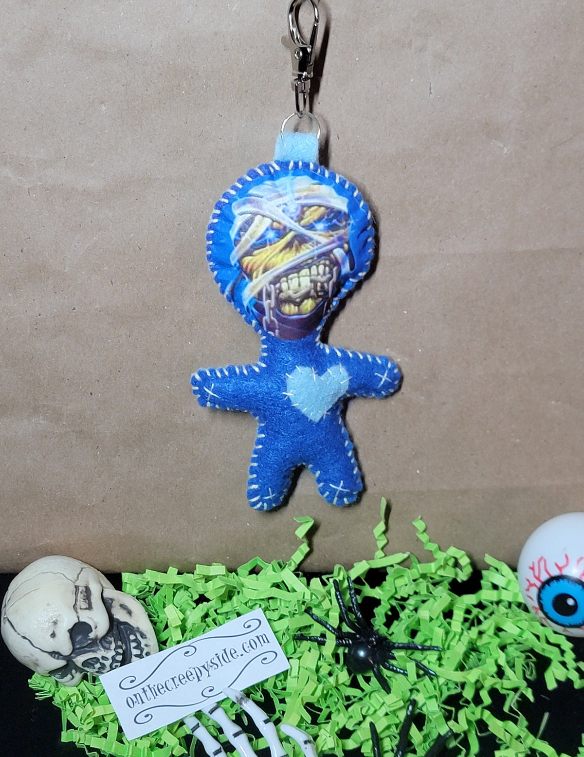 Front view of handmade blue felt mummy Rock Mascot Stitchling keychain with wrapped face and pale blue heart