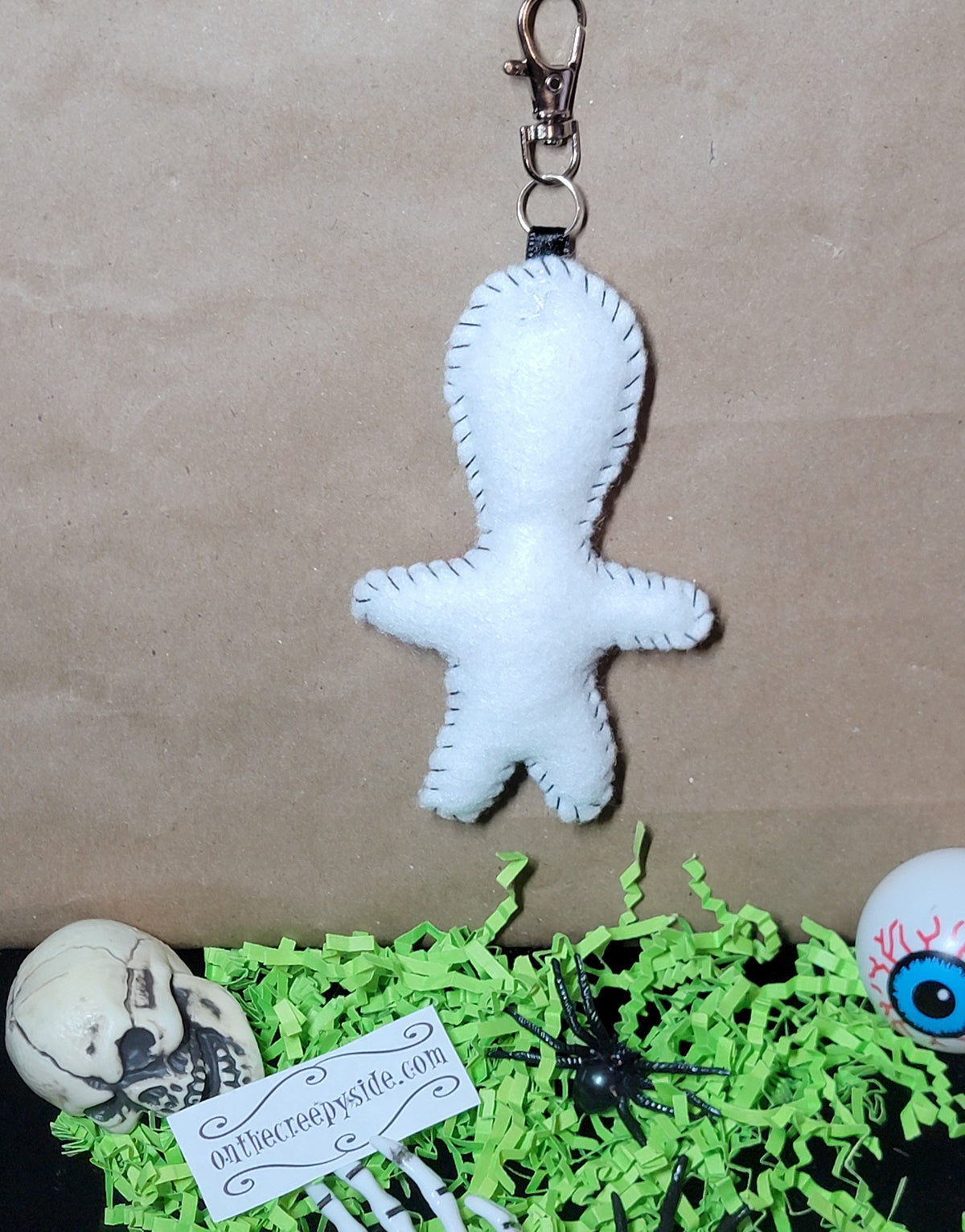 Back view of handmade white felt Rock Star Stitchling keychain showing black hand-stitched edging and metal clip