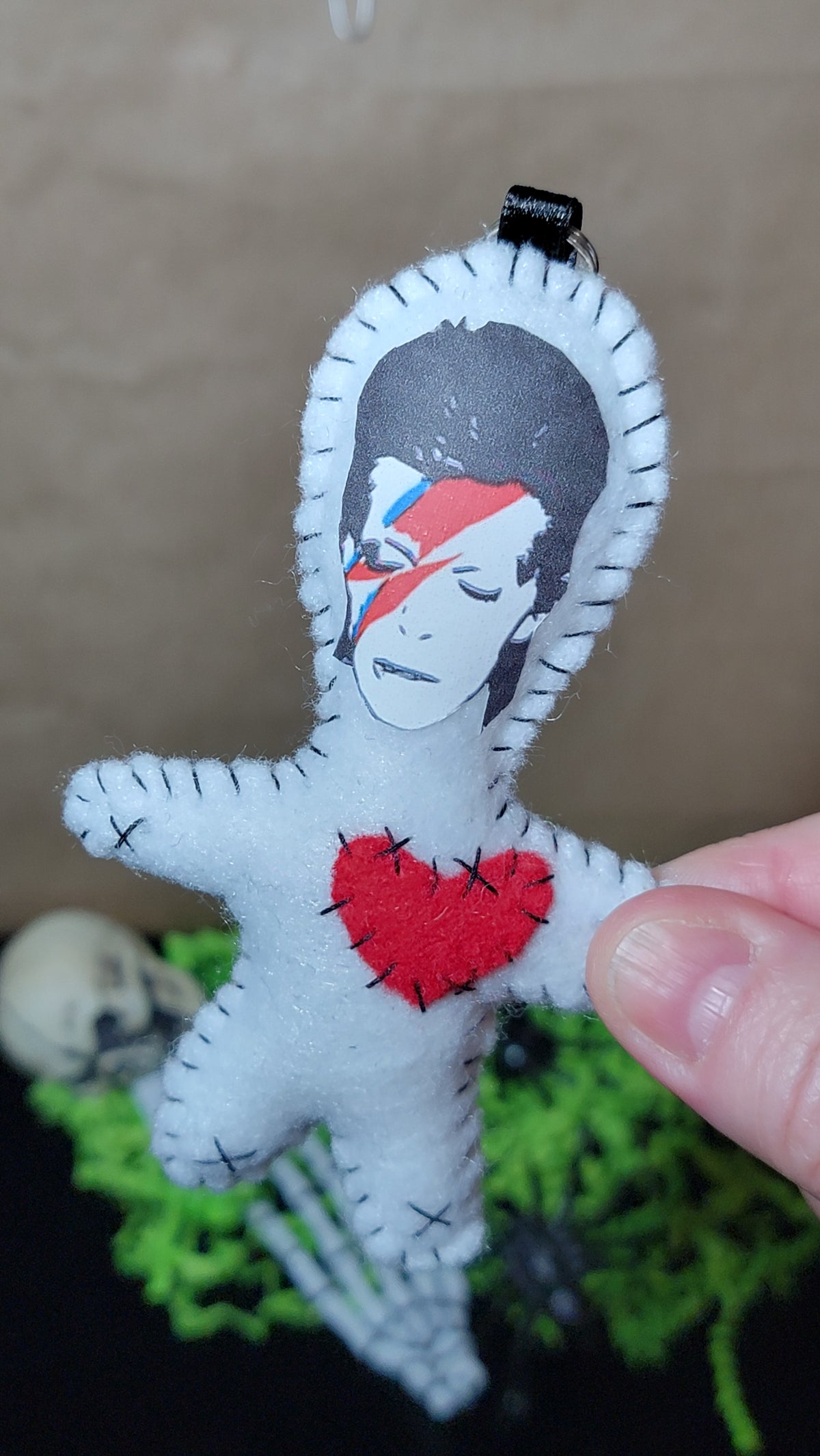 Close-up of handmade white felt Rock Star Stitchling keychain with red-and-blue lightning-bolt face and stitched red heart