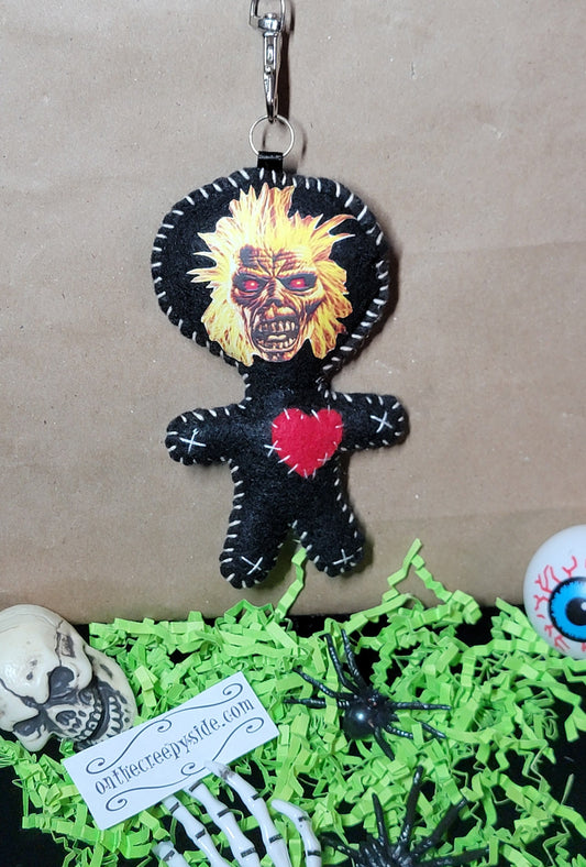 Close-up of handmade black felt Music Mascot Eddie Stitchling keychain with yellow hair, red eyes, and stitched red heart