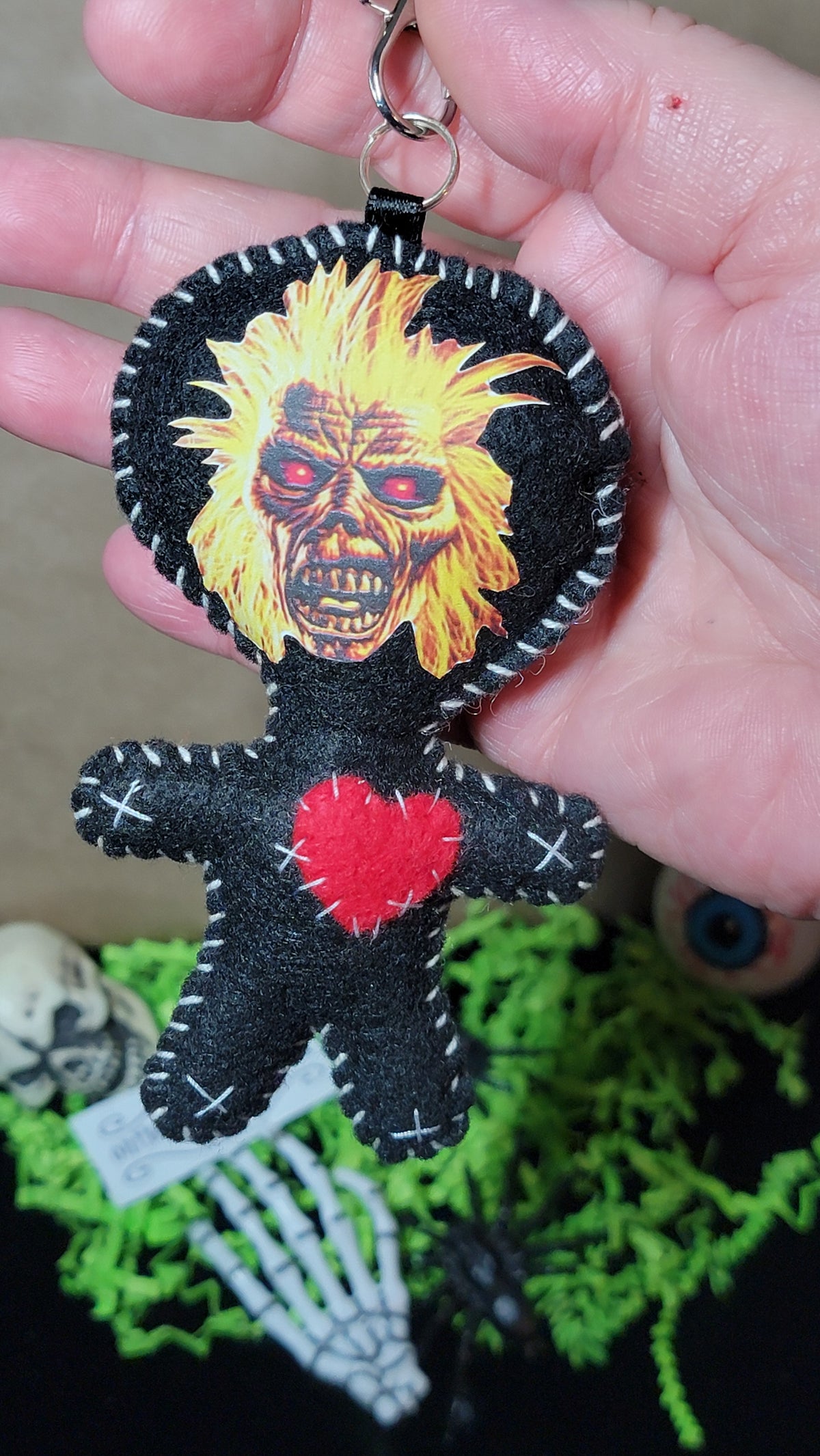 Front view of handmade Music Mascot Eddie Stitchling black felt keychain with metal clip, white stitching, and red heart
