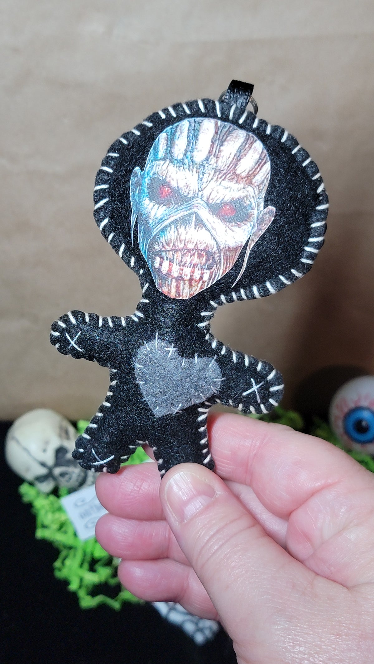 Close-up of handmade Eddie Stitchling felt keychain showing a silver monster face, red eyes, white stitching, and gray heart⠋