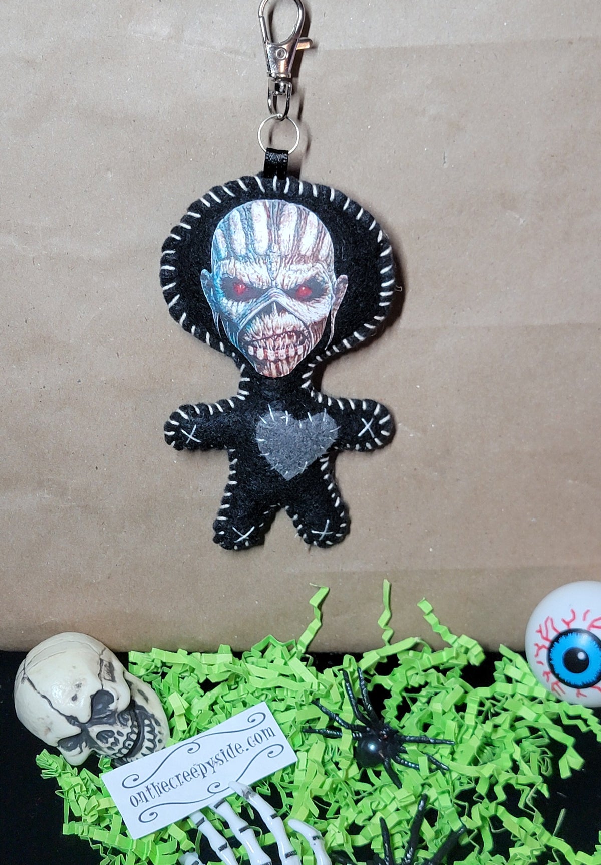 Front view of handmade black felt Eddie Stitchling keychain with silver monster face, red eyes, and gray stitched heart