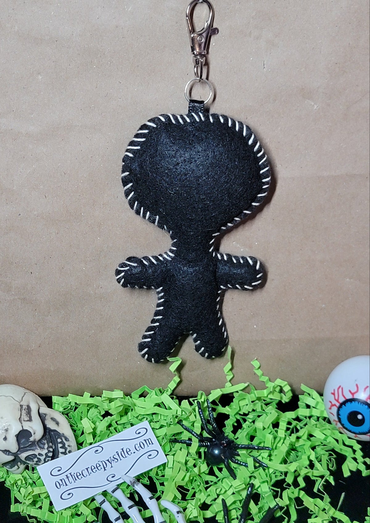 Back view of handmade black felt punk rock skull Stitchling keychain with white hand-stitched edging and metal clip