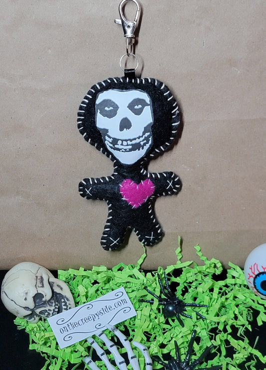 Front view of handmade black felt punk rock skull Stitchling keychain with white stitching and a hot pink heart
