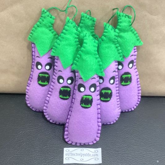 Purple felt eggplant plush toys with green stems , displayerd on a gray surface.